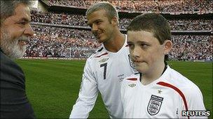 England mascot Robert Sebbage (R) watches Brazil's President Luiz Inacio Lula da Silva (2nd L) greet England's David Beckham