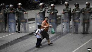 An unidentified woman passes with a child near a line of National Guard soldiers outside El Rodeo II prison in Guatire, Venezuela, Tuesday June 21, 2011.