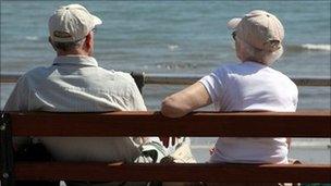 An elderly couple sitting on a bench and looking out to sea