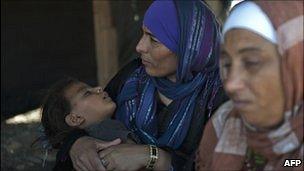 Bedouin women, one holding her daughter, inside a makeshift structure.