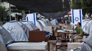 Protestor with a megaphone among rows of tents.