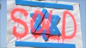 Protest sign reading "sold" over Israeli flag.