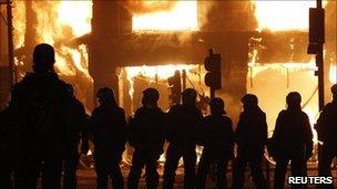 Police stand in front of a burning building