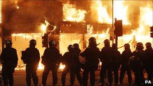 Line of riot police stand in line as fire rages through a building in Tottenham