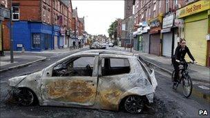 A woman cycles past a burnt out car on Lawrence road in Wavertree