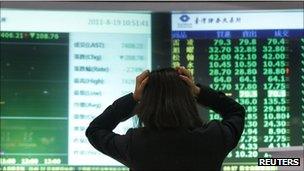 Woman holding her head in front of screens with market prices