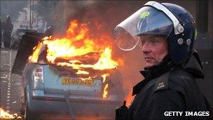 A police officer in riot gear stands near a burning car in Hackney on 8 August