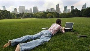 Man uses laptop in park with view of city in background