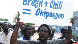 Haitian protesters, one brandishing a placard reading "Brazil plus Chile equals occupation".