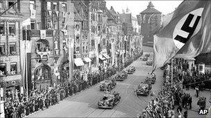 Adolf Hitler salutes supporters from a car as he passes through Nuremberg, 5 September 1938