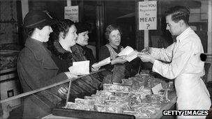 A butcher cuts a coupon out of a customer's ration book in South London, 1940