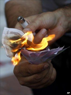 A protester uses a burning 10 euro banknote to light up fake euro banknotes during an anti-austerity protest in front of Greeces" central bank in Athens in September