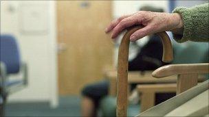 Elderly patient rests her hand on her walking stick in a waiting room