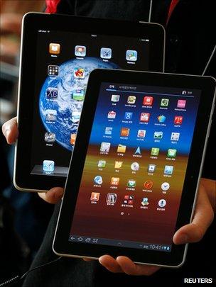 A shop employee holds an Apple iPad behind a Samsung Galaxy Tab