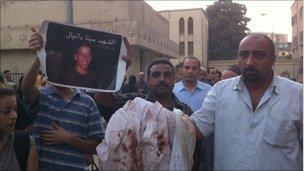 A man shows the bloodstained clothes of Mina Daniel outside St Mark's Cathedral. Photo by Hamada Abu Qammar