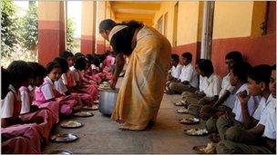 A lady serving food to school kids