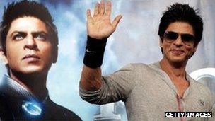 Shah Rukh Khan poses in front of a poster for his film Ra.One