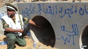 An NTC fighter points to a drainage pipe in which Col Muammar Gaddafi is said to have been captured, Sirte, 20 October 2011