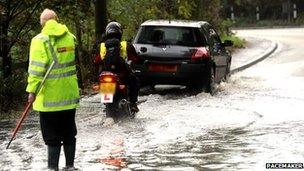 DoE worker in flooded road with motorcycle and car