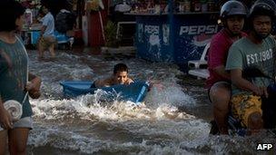 A boy in a boat is towed up a Bangkok street by a motor bike