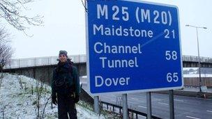 Rob Lilwall standing next to a road sign on a verge of the M25