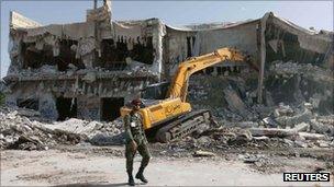 A soldier walks past the house of former leader Muammar Gaddafi as it is demolished by a bulldozer in Tripoli