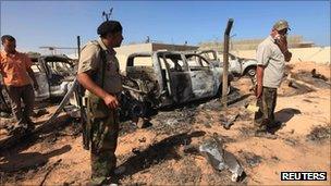 Anti-Gaddafi fighters stand in front of damaged cars after an attack by Nato on Gaddafi's convoy in Sirte