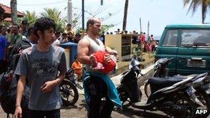 In this handout photograph released by Pikiran Rakyat, an unidentified survivor carrying a child is escorted at a marine police station on the coast of Pangandaran town in Indonesia's West Java province on November 1