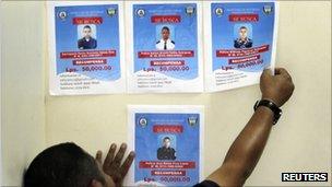 A man puts up wanted posters for four Honduran policemen accused of killing two students