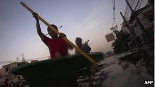 A boy and man row their boat through a flooded neighbourhood in Bangkok November 3