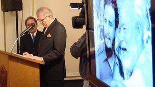 Cuban diplomat speaks at a podium in front of a photo of Fidel Castro and Ernest Hemingway