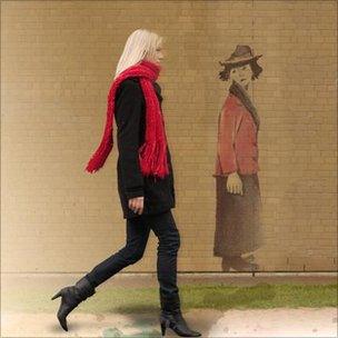 Woman walking past Lowry type figure on wall