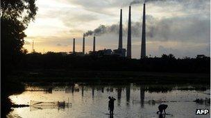 Indian labourers prepare a flooded field for rice farming in front of chimneys of Kolaghat Thermal Power Plant in Mecheda