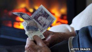 An elderly person holds cash facing a fire