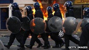 Line of police officers in riot gear walking past a burning car in Hackney on August 8 2011 in London