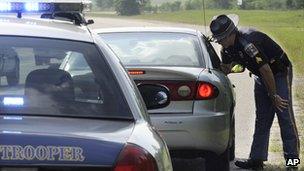 A police man talks to a driver in a vehicle. The police cruiser is in the foreground.