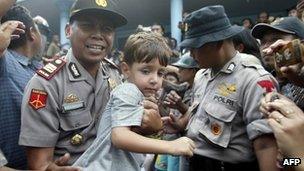 An Indonesian police carries a young survivor while officials transfer them to an immigration office, in Watulimo on 18 December 2011