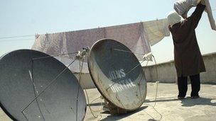 Iranian woman hanging washing next to satellite dishes