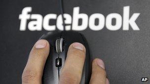 A hand on a mouse atop a Facebook logo mousemat