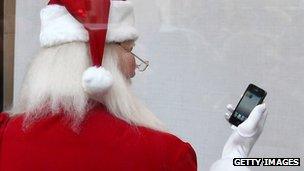 A man dressed as Father Christmas holds an iPhone