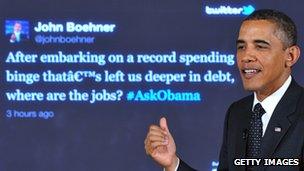 Barack Obama in front of a screen displaying a tweet