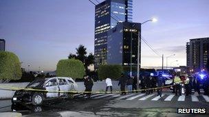 Police officers work at a crime scene where the dead bodies of two men, left inside a burning vehicle, were found near a mall on the outskirts of Mexico City 11 January, 2012