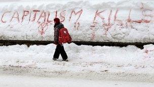 A girl walks past the slogan "Capitalism Kills" written in the snow, Davos