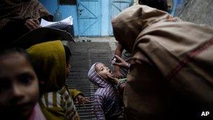 A child is administered polio drops by health workers at his residence during a door to door drive in Delhi