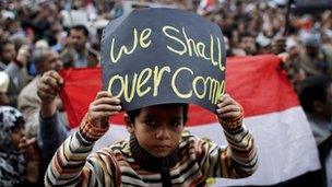 An Egyptian boy poses with a sign in front of anti-government protesters in Tahrir Square