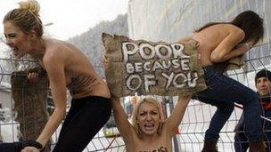 Topless female protesters holding a sign saying "poor because of you"