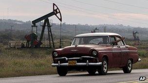 A man waves from his car as he drives by oscillating oil pumps operated by the state oil company Cuba Petroleos, January 2012