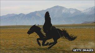 A herder rides his horse at a field under the Tianshan Mountain