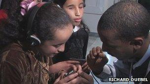 A man explains to blind and partially-sighted children how to use special headsets designed to allow intrusive commentary on a film. Photo by Richard Duebel.