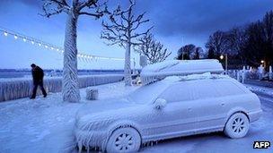 A man walks past an ice covered car on the frozen waterside promenade at Lake Geneva, Switzerland